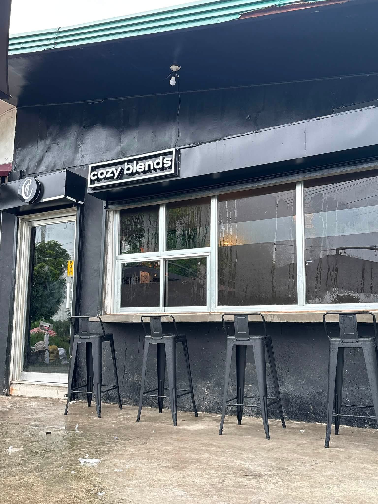 The black cozy blends storefront with its boxed sign, round logo, and bar stools along the window